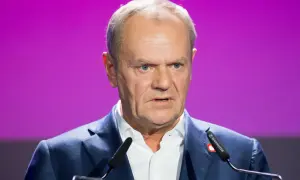 Donald Tusk, polityk o charakterystycznym wyglądzie, przemawia na tle fioletowej sceny. Jego wzrost jest imponujący, a pewność siebie emanuje z każdego gestu.