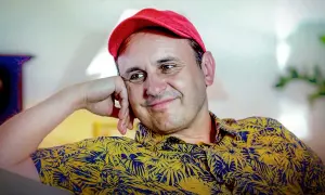 Uśmiechnięty Adam Woronowicz w czerwonej czapce i żółtej koszuli w liście. Wiele jego filmów zapisało się w pamięci widzów.