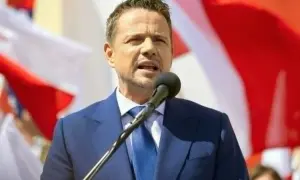 Bartosz Kopania przemawia do tłumu na tle biało-czerwonych flag.