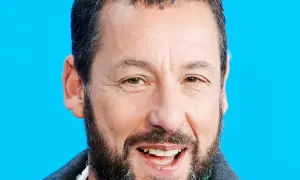 Uśmiechnięty Adam Sandler, gwiazda wielu komediowych filmów, na tle niebieskiego tła.