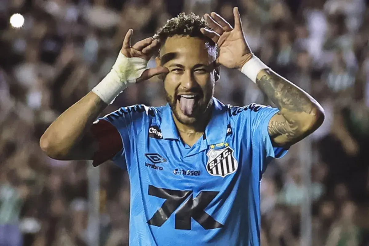 Neymar w niebieskiej koszulce Santos, z językiem na wierzchu i rękami przy oczach, celebruje bramkę.