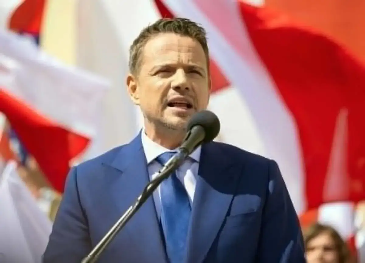 Bartosz Kopania przemawia do tłumu na tle biało-czerwonych flag.
