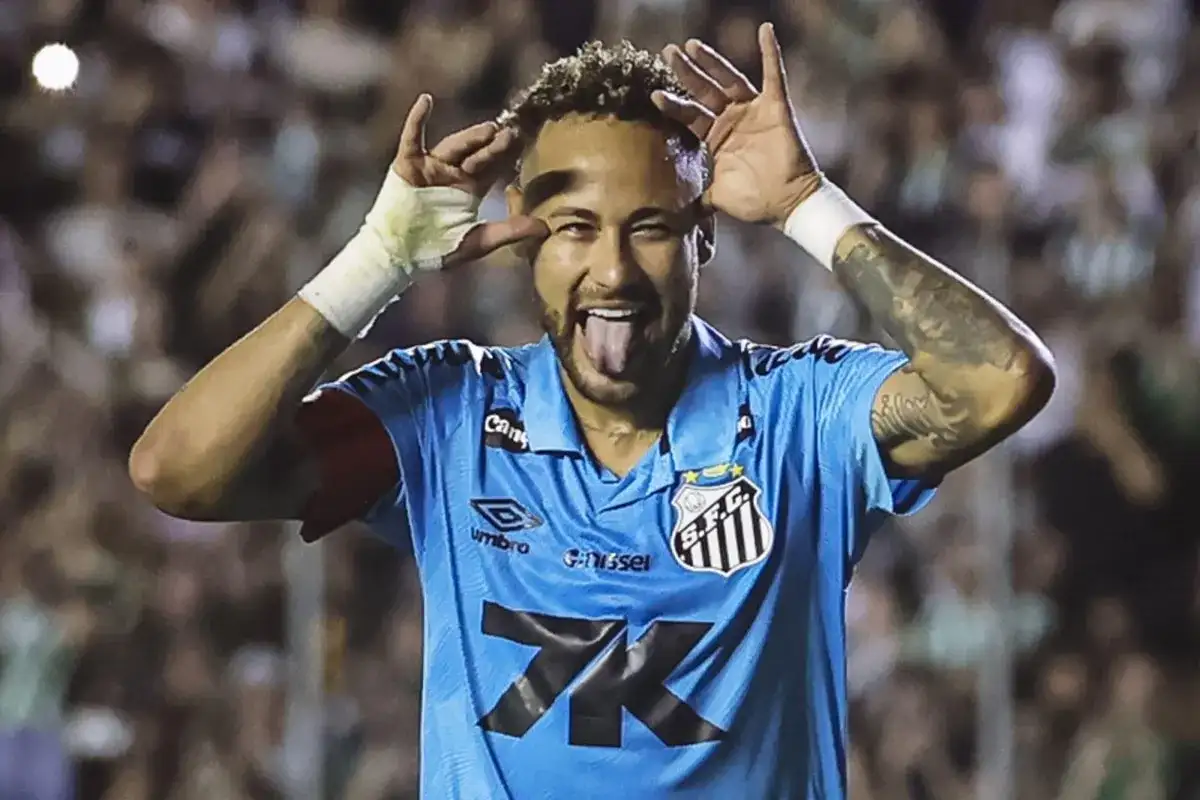 Neymar w niebieskiej koszulce Santos, z językiem na wierzchu i rękami przy oczach, celebruje bramkę.