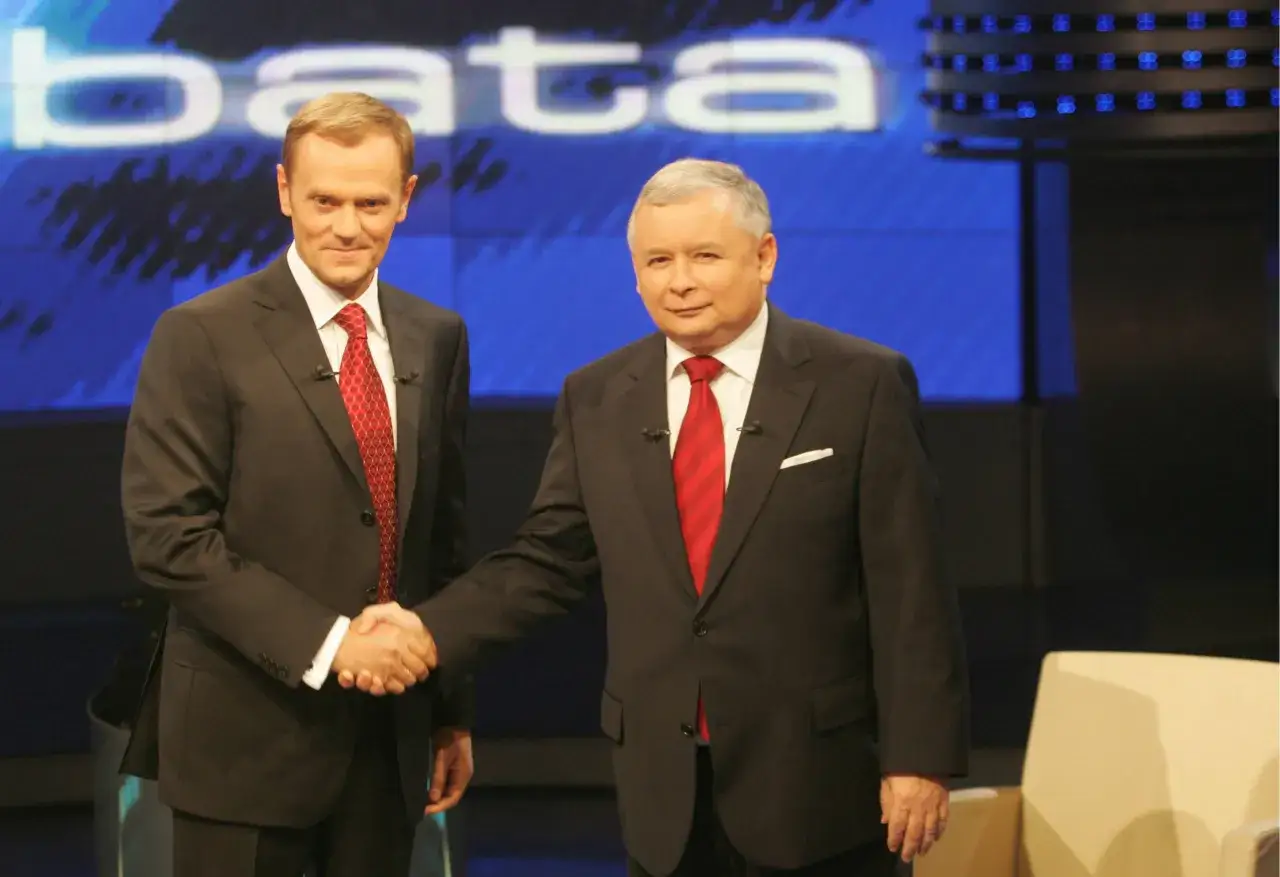 Jarosław Kaczyński i Donald Tusk podają sobie ręce. Wzrost obu polityków jest podobny, choć Kaczyński wydaje się nieco niższy.