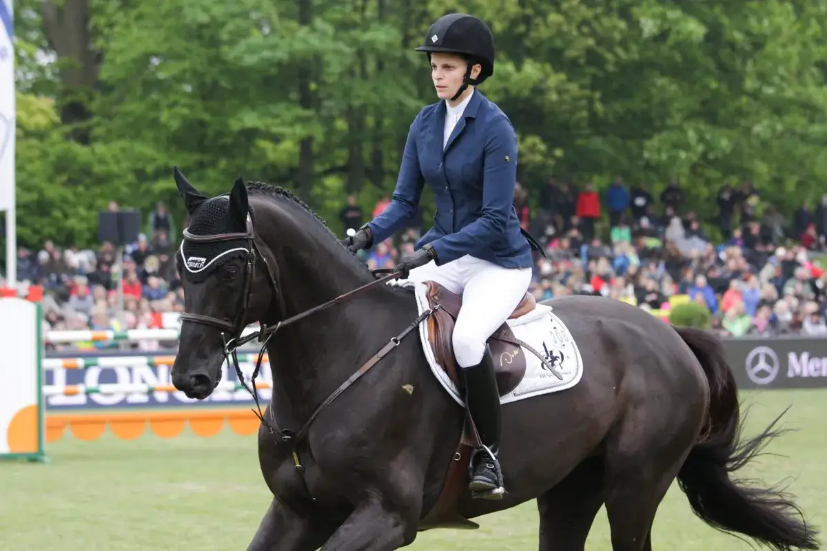 Athina Onassis w ciemnej marynarce i białych bryczesach dosiada czarnego konia podczas zawodów jeździeckich.
