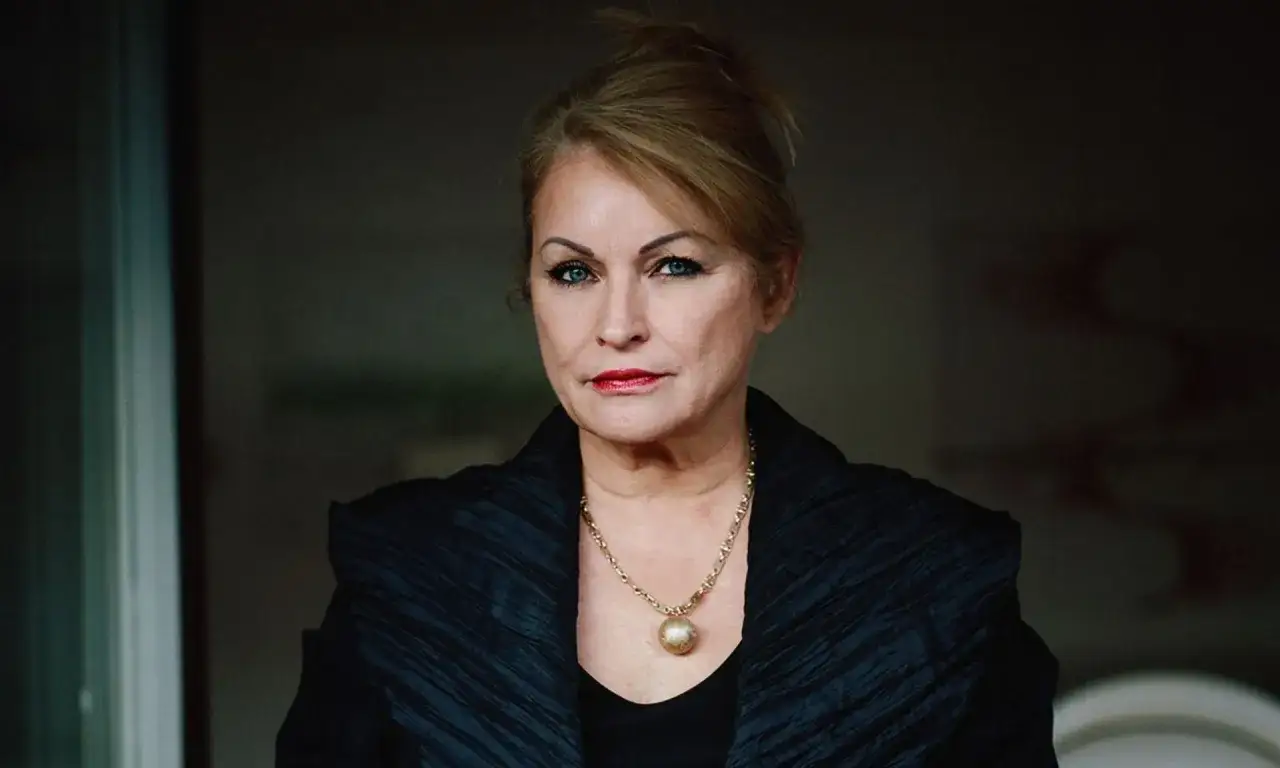 Grażyna Dyląg, żona, w czarnej, eleganckiej kreacji z złotym naszyjnikiem, patrzy prosto w obiektyw.