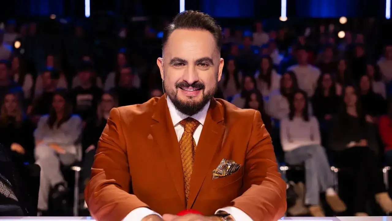 Uśmiechnięty Augustin Egurola w pomarańczowej marynarce, z widownią w tle.