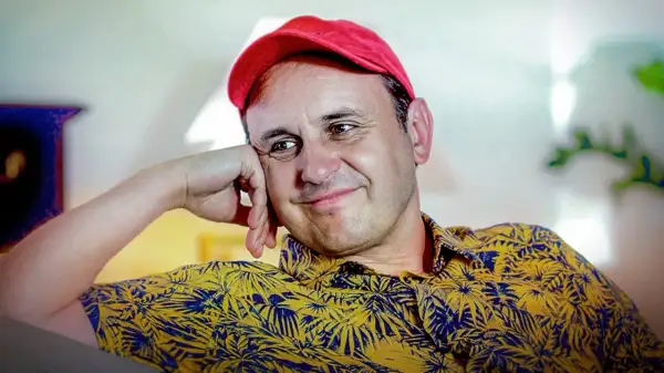 Uśmiechnięty Adam Woronowicz w czerwonej czapce i żółtej koszuli w liście. Wiele jego filmów zapisało się w pamięci widzów.