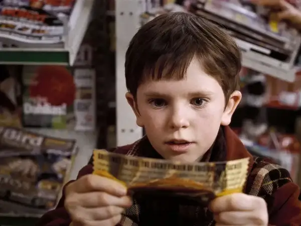 Chłopiec z filmu "Charlie i fabryka czekolady" trzyma złoty bilet. Freddie Highmore w tej roli to początek jego kariery w filmach, serialach i programach.