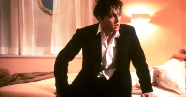 Hugh Grant w garniturze, w rozpiętej koszuli, wygląda na zamyślonego. Scena z jednego z jego filmów.