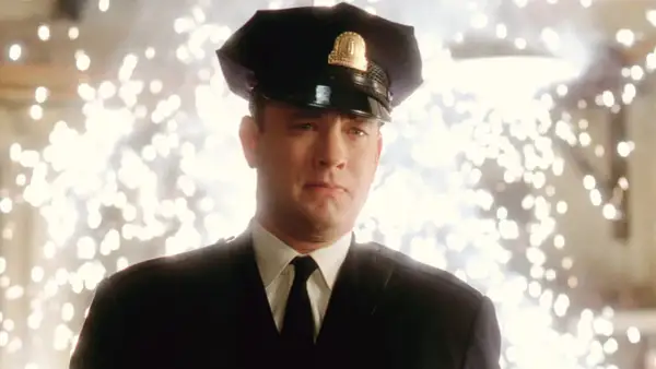 Tom Hanks w mundurze strażnika w jednym z jego filmów. Tło rozświetlone jest fajerwerkami.