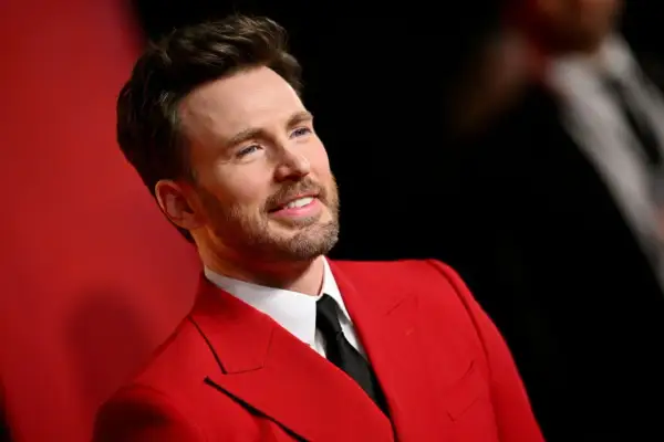 Chris Evans w czerwonym garniturze, jak z najlepszych filmów. Uśmiechnięty, z zarostem, prezentuje się elegancko.