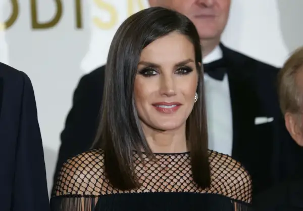 Elegancka królowa Letizia w czarnej, siateczkowej kreacji, z błyszczącymi oczami i uśmiechem, pozuje do zdjęcia z innymi osobami.