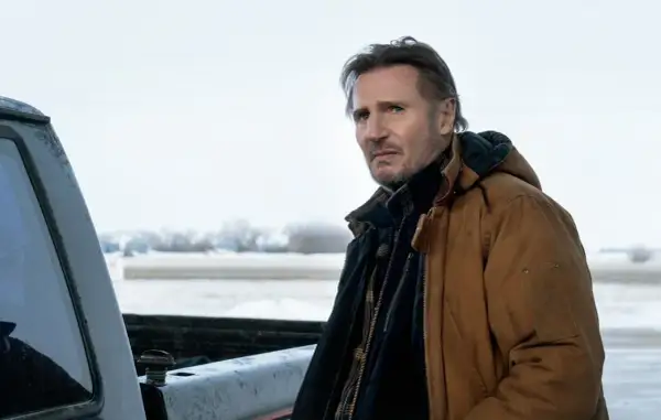 Liam Neeson w brązowej kurtce, w zimowej scenerii, jak w jego filmach.