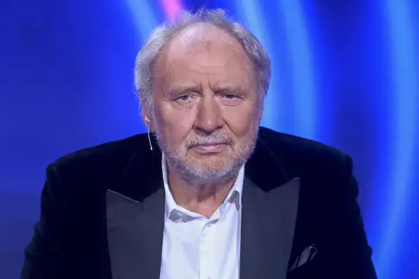 Andrzej Grabowski, znany z wielu niezapomnianych ról w polskich filmach, w eleganckim czarnym garniturze na tle niebieskiego światła.